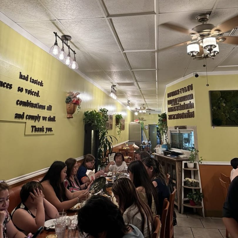 Diners seated at tables in a brightly lit Tamarind Thai Cuisine restaurant with yellow walls and ceiling fans.
