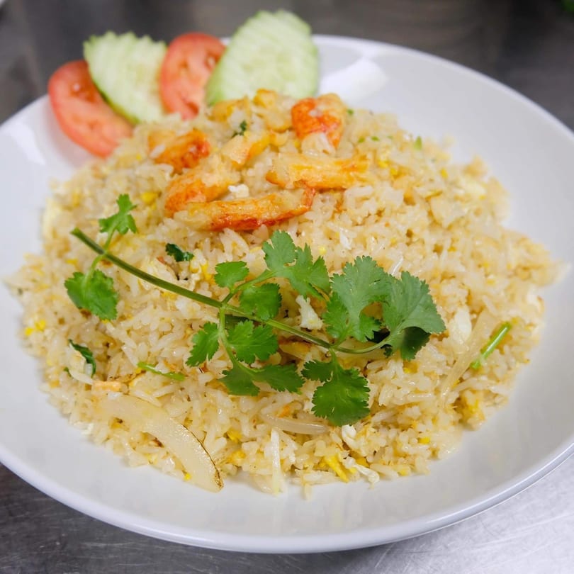 Thai fried rice with shrimp, egg, and vegetables, garnished with cilantro, cucumber, and tomato slices.